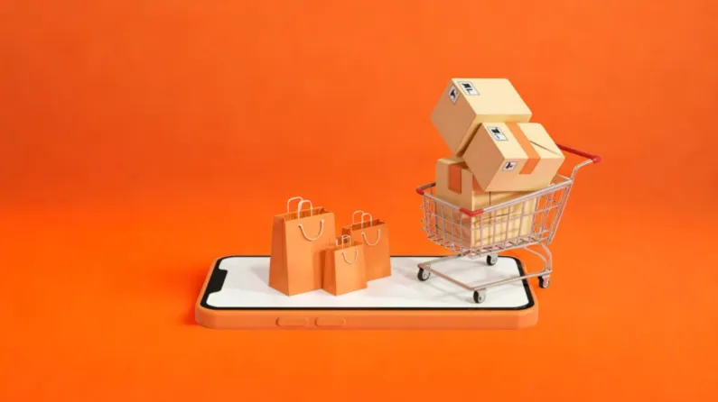 Miniaturas de sacolas de compras e um carrinho cheio de caixas de papelão estão posicionados sobre a tela de um smartphone em um fundo laranja.