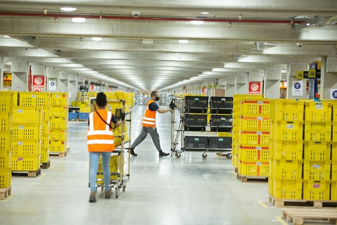 imagem do centro de distribuição do Mercado Livre com funcionários empurrando carrinhos de produtos entre as ilhas de caixotes de produtos