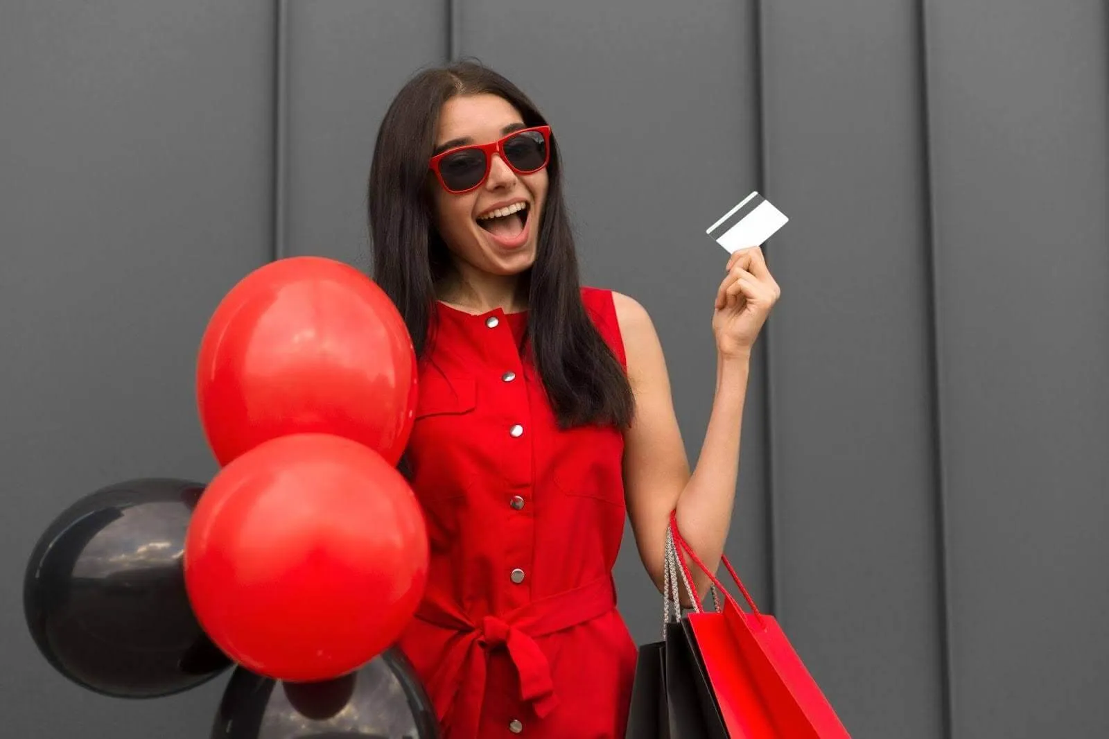 Mulher segurando balões vermelhos e cartão de crédito