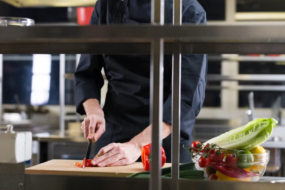 imagem de uma pessoa trabalhando picando vegetais em uma cozinha industrial 