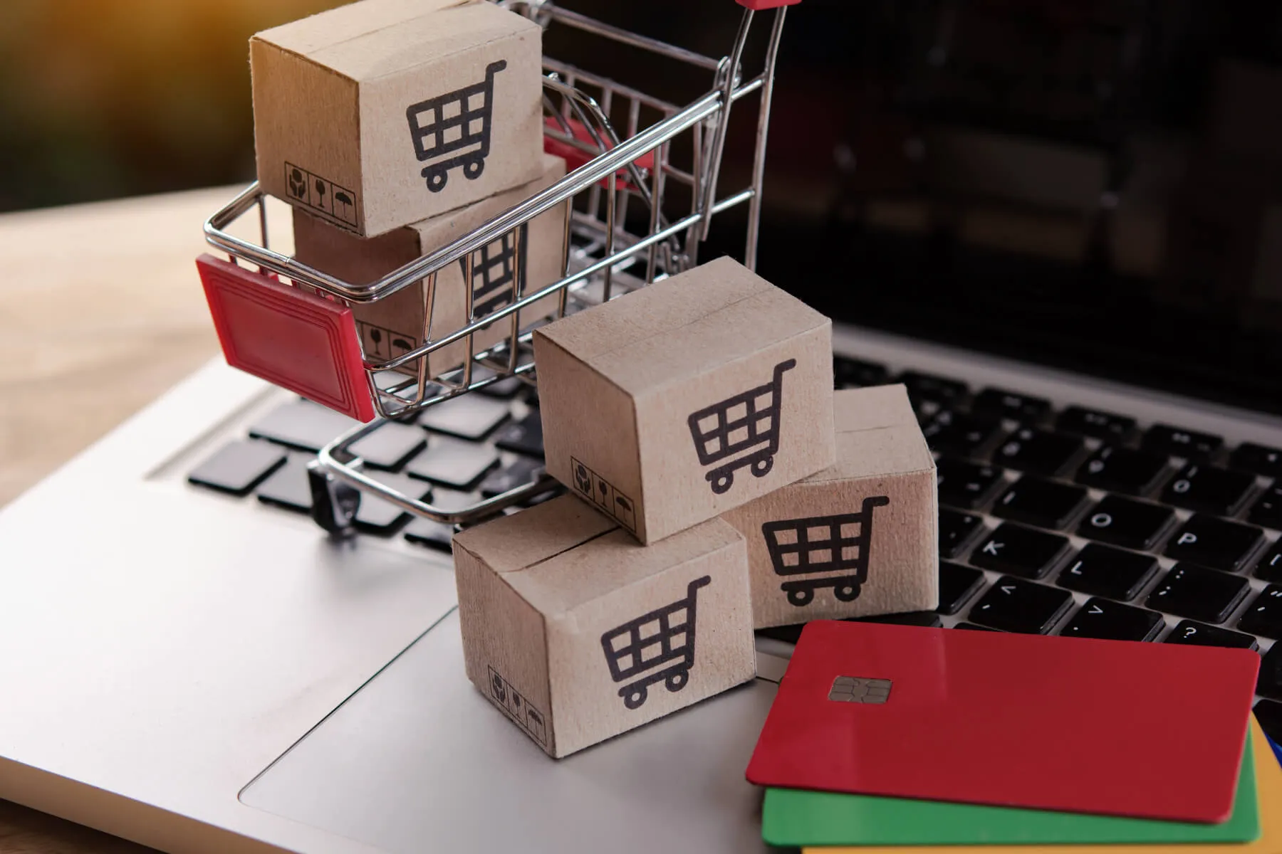 Carrinho de compras em miniatura em cima de um computador com pequenos blocos de madeira com carrinho de compras desenhados