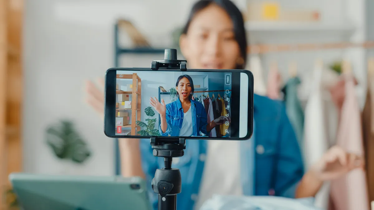 Mulher japonesa de cabelo escuro está gesticulando em frente a um smartphone que está em cima de um tripé a filmando.