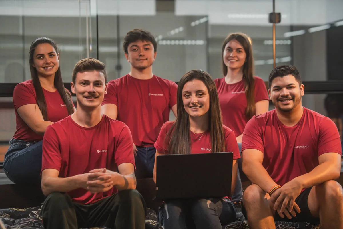 Equipe da empresa Magazord sentada em frente ao computador uniformizados com camiseta vermelha