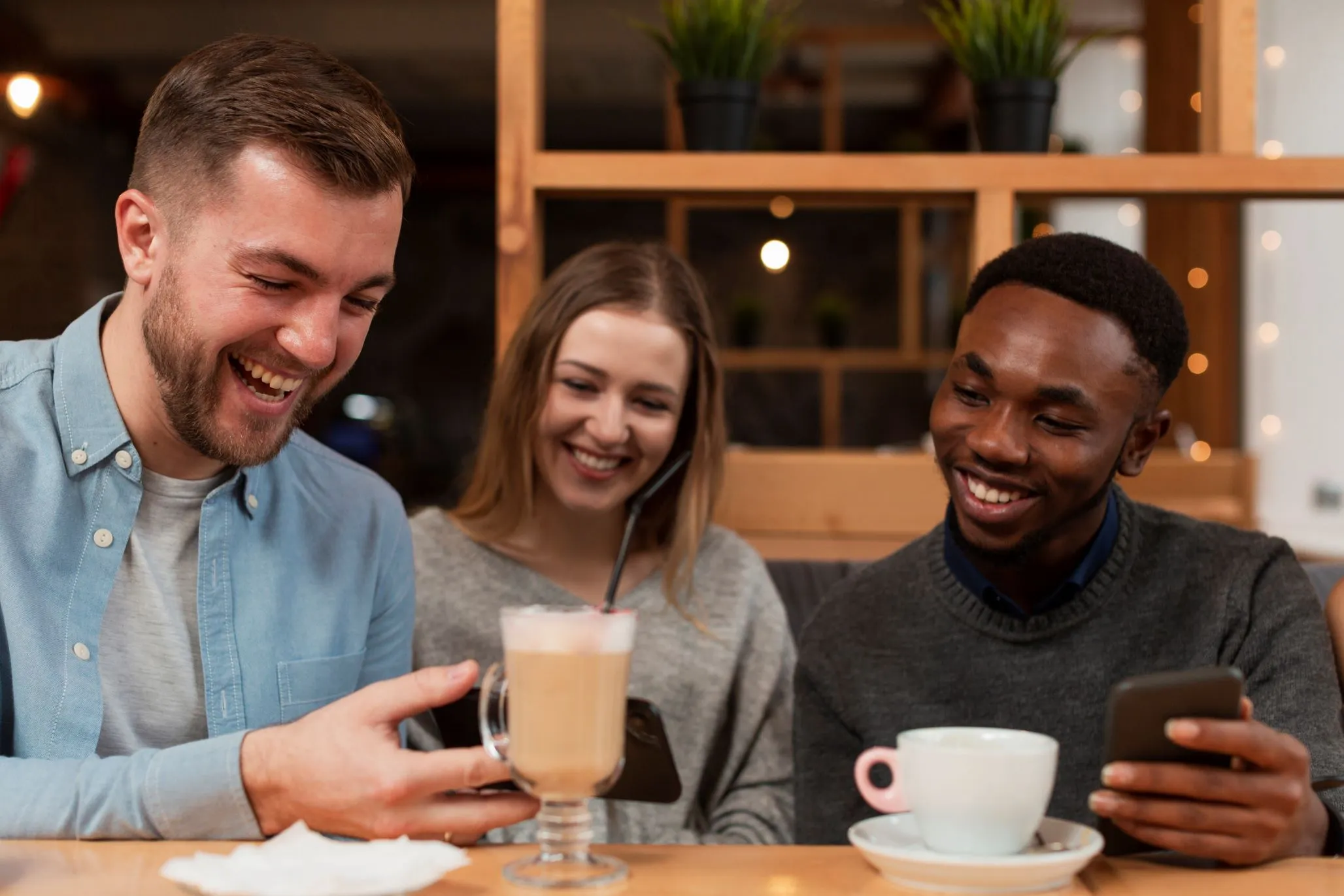 Três amigos jovens sorrindo para um celular no café