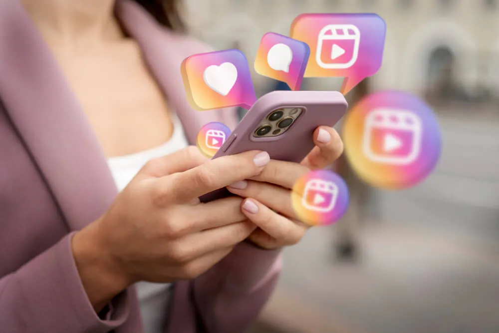 Mulher vestindo terno cor de rosa mexendo em celular com ícones do Instagram flutuando em volta do aparelho