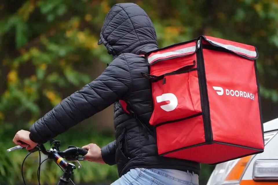 Homem com casaco e capuz em bicicleta com mochila de entregas de comida da DoorDash