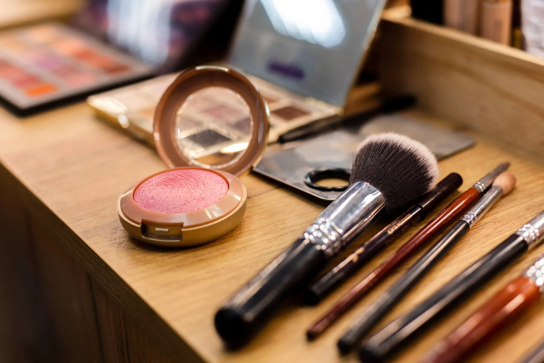 Pincéis de maquiagem, paleta de sombras e blush em cima de mesa de mandeira