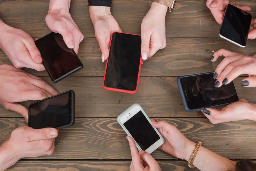 Pessoas segurando celulares em cima de mesa de madeira