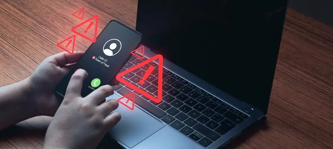 Pessoa recebendo ligação suspeita no celular enquanto senta de frente para computador