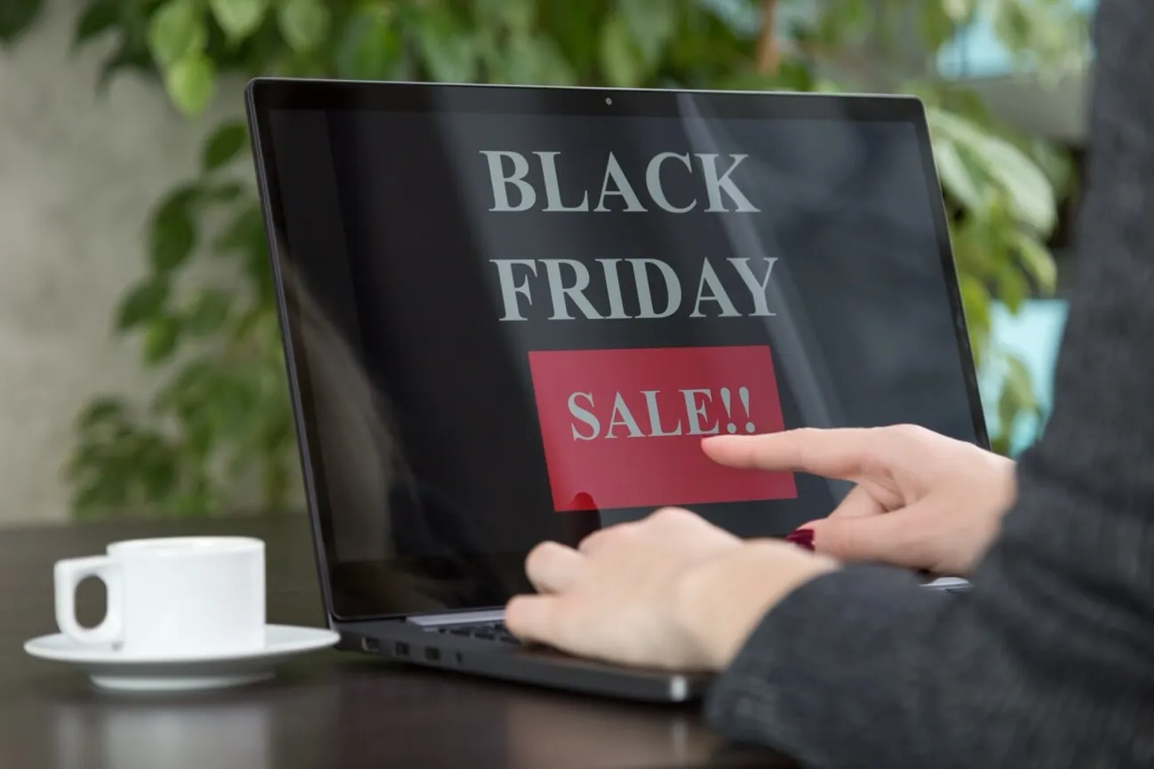 Consumidor olhando para computador com xícara ao lado e Black Friday Sale escrito na tela