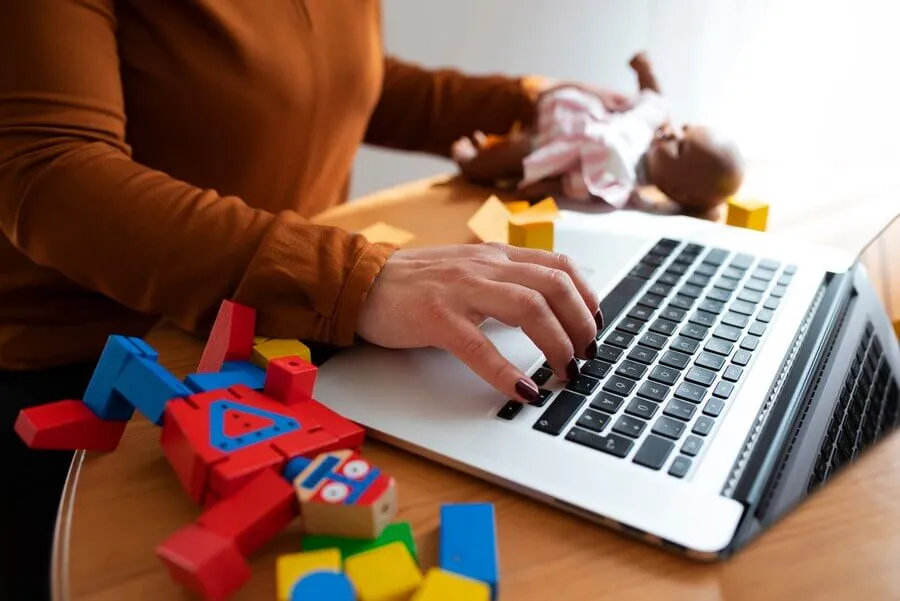 Mulher pesquisando brinquedos no computador com blocos de madeira ao lado