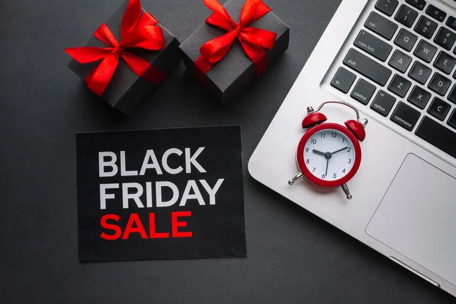 Placa escrito Black Friday Sale ao lado de computador e caixas de presente com laço vermelho