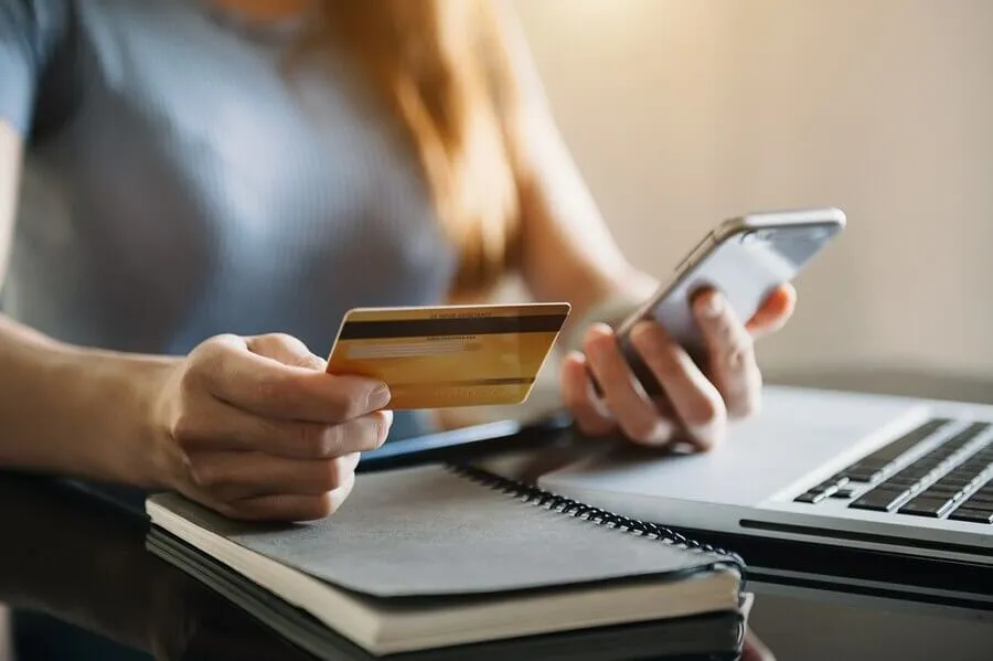 Mulher cadastrando cartão de crédito no celular em frente ao computador