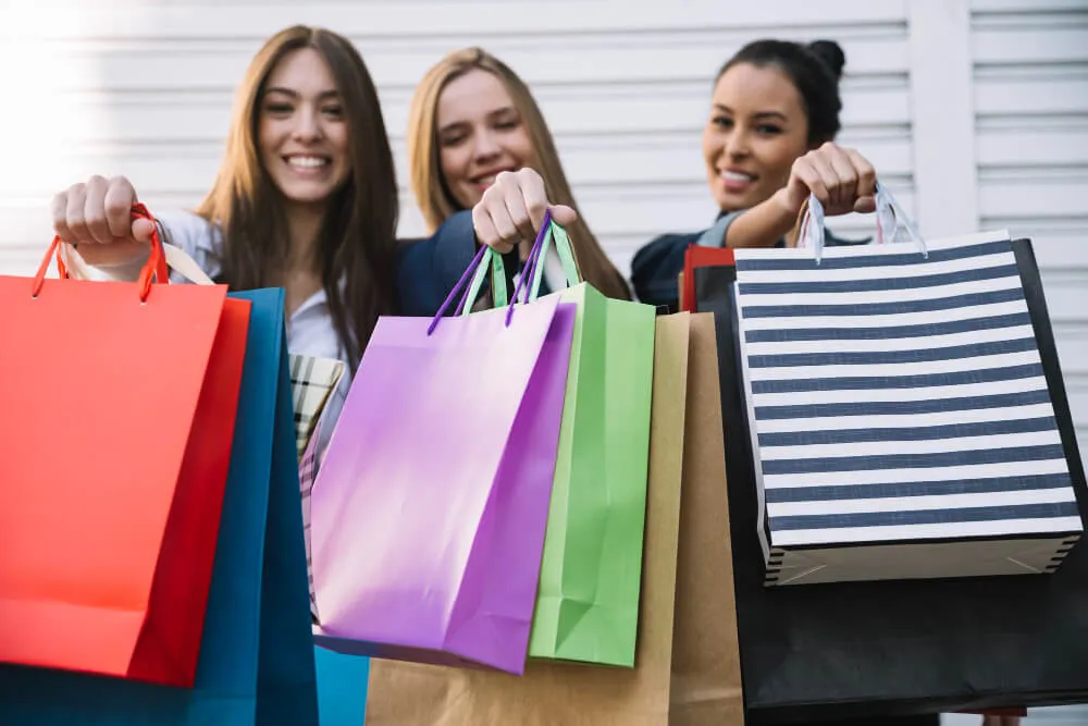 Grupo de amigas segurando sacolas e sorrindo para camera