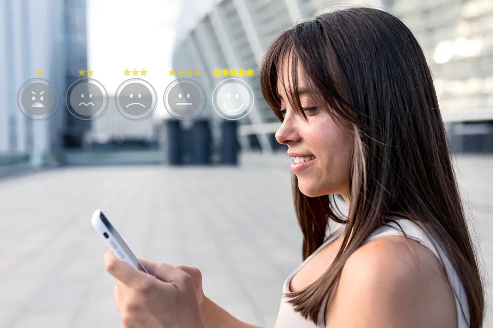 Mulher sorrindo ao usar o celular, com ícones de avaliação de satisfação acima dela, destacando uma resposta positiva.
