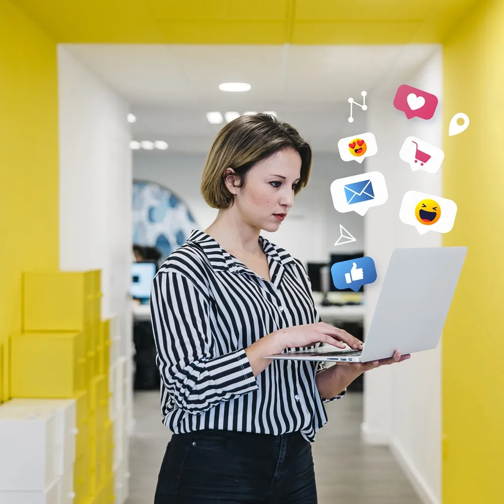 Mulher usando laptop em escritório com ícones digitais flutuantes representando redes sociais e marketing online.