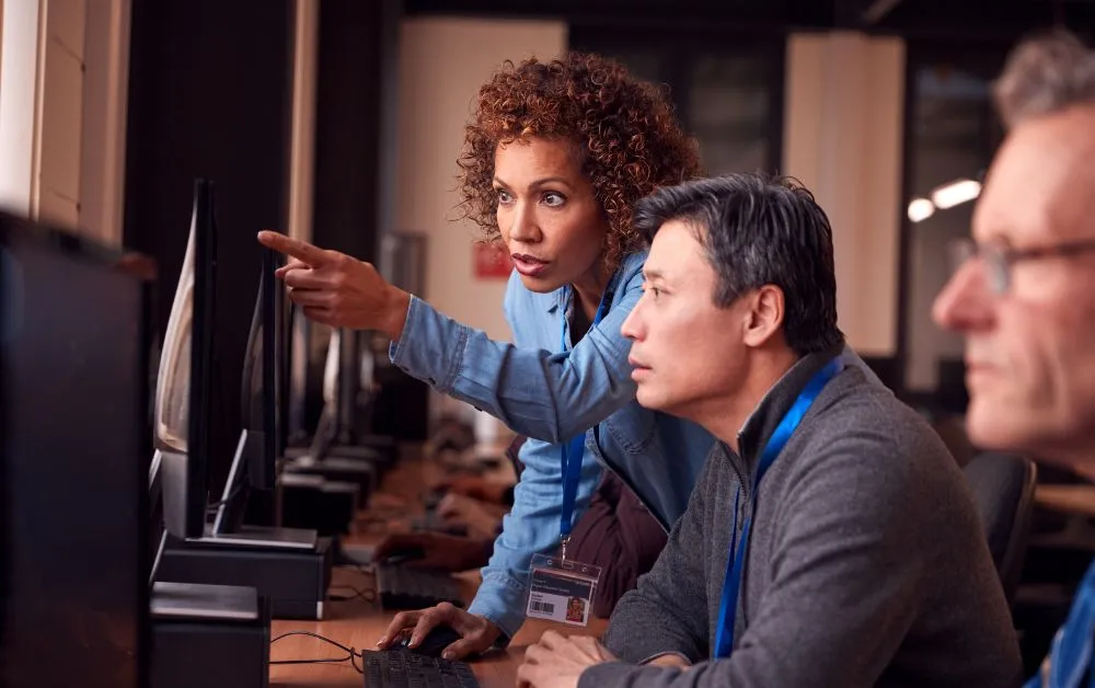 Mulher orienta homem na frente de um computador.