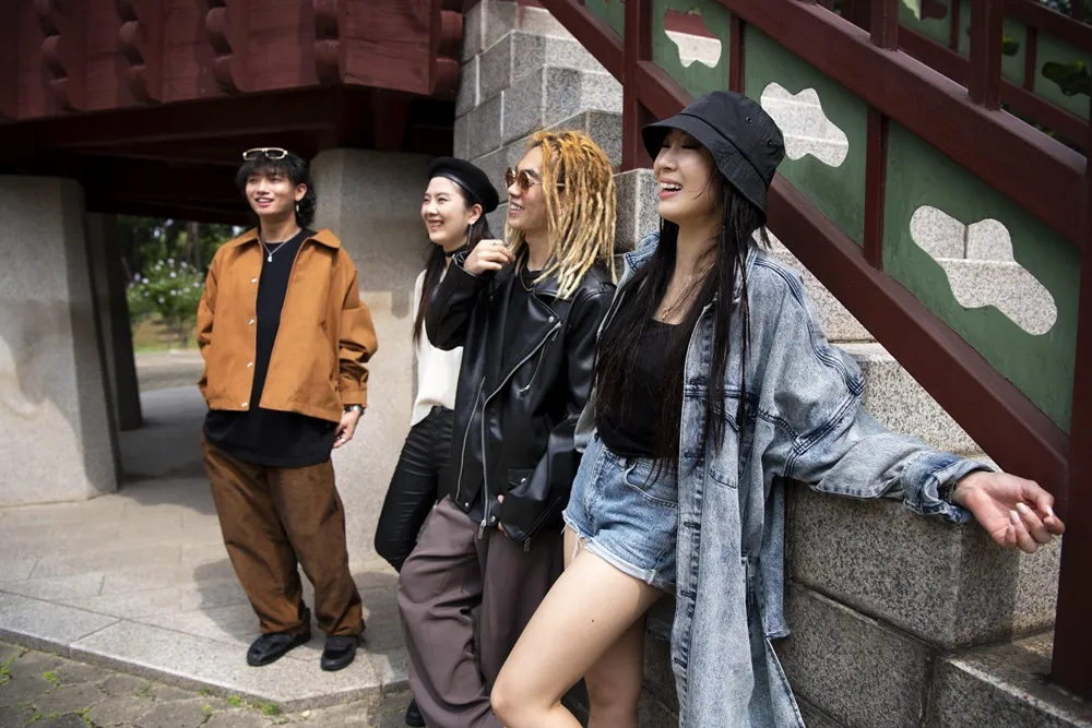 Pessoas sorrindo ao ar livre, vestidas com looks urbanos e modernos, em frente a uma construção.