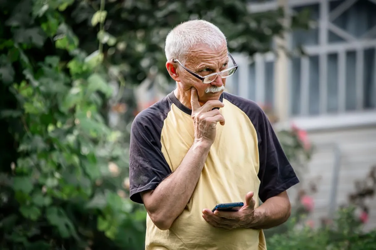 Idoso pensativo mexendo no smarpthone