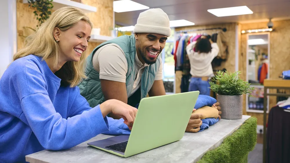 Pessoas sorrindo enquanto analisam algo em laptop em loja de roupas.
