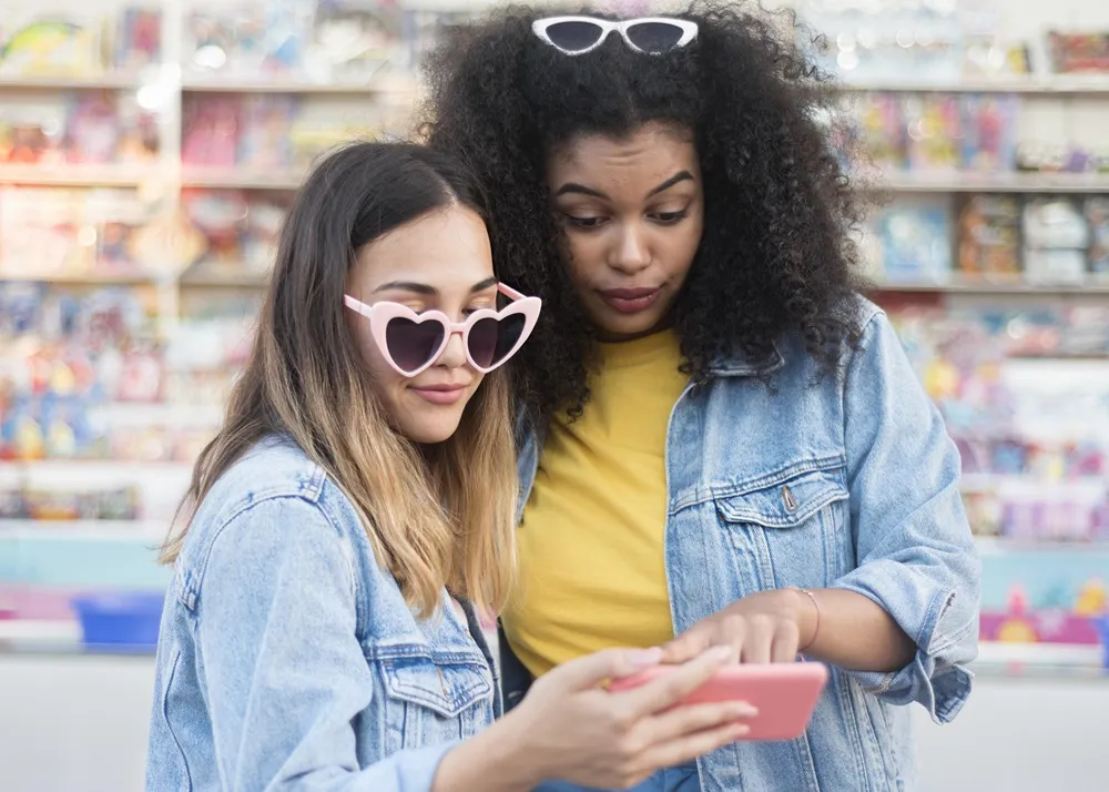 Duas jovens com óculos estilosos olham para um celular em uma loja.